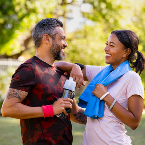 A lively athletic couple smiling and laughing in the sunshine at a park exercising