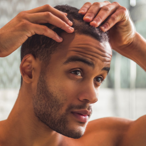 Close up of man's face looking at his scalp, with his hands combing through his hair