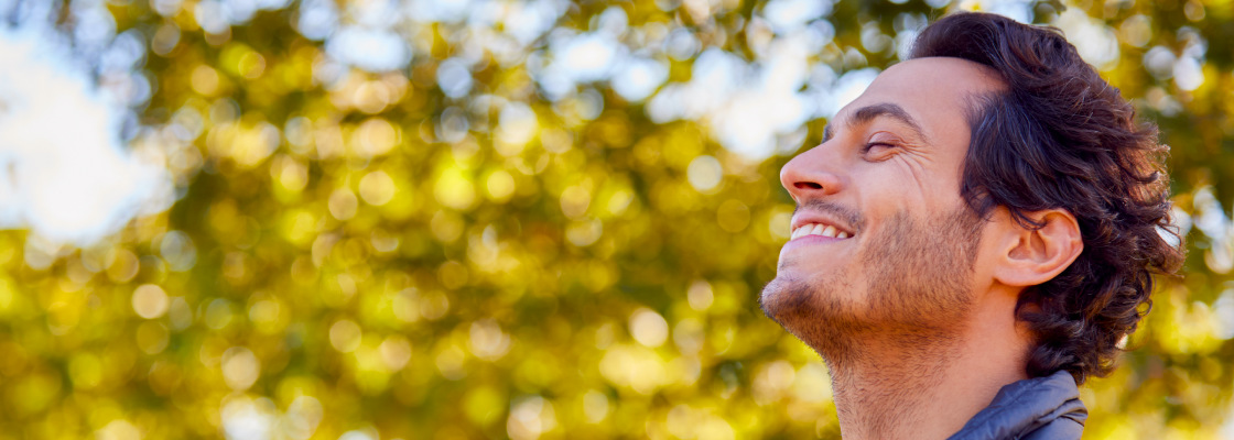 Man facing upward smiling who is feeling relieved and content while spending time outdoors