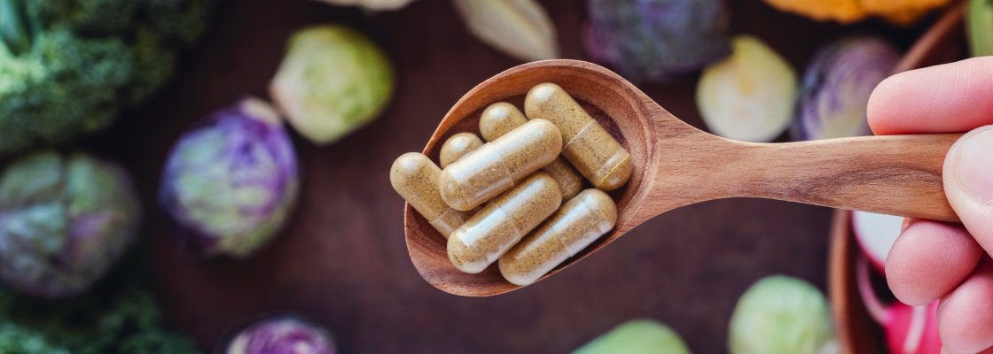 Top down view of a spoon full of supplements, over a table of vegetables below