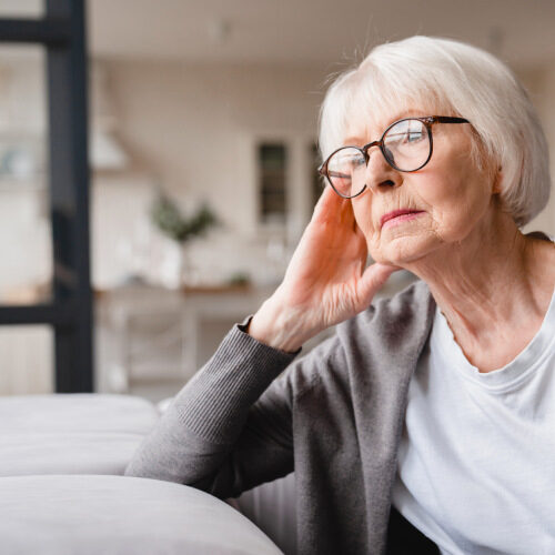 Worries woman with glasses, sitting on couch looking out with a blank stare