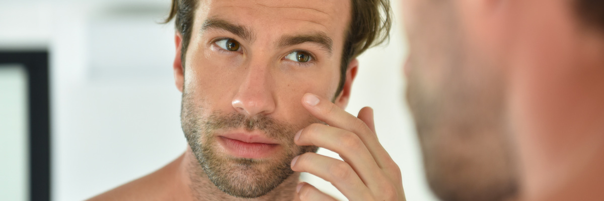 Man is inspecting his own face skin texture with finger in the mirror