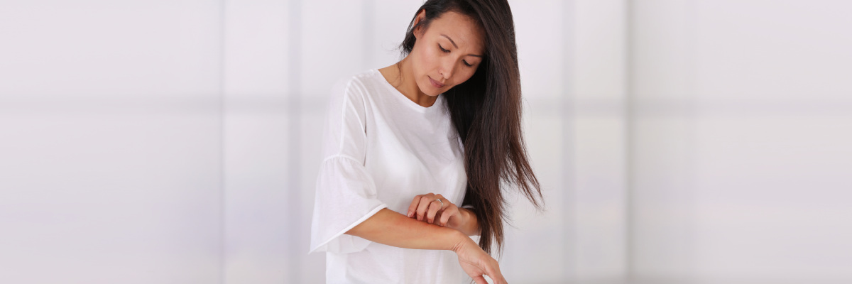 Woman standing scratching her right arm