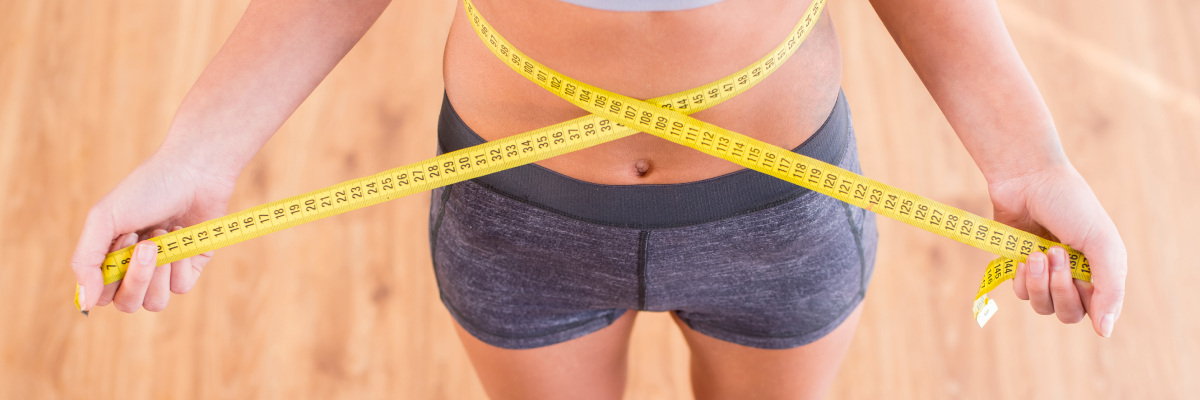 A woman holding a yellow measuring tape around her waist 