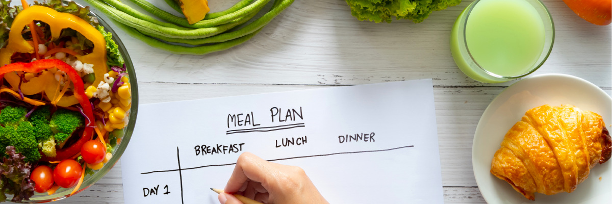 Top view of hand filling meal plan surrounded by different foods on table